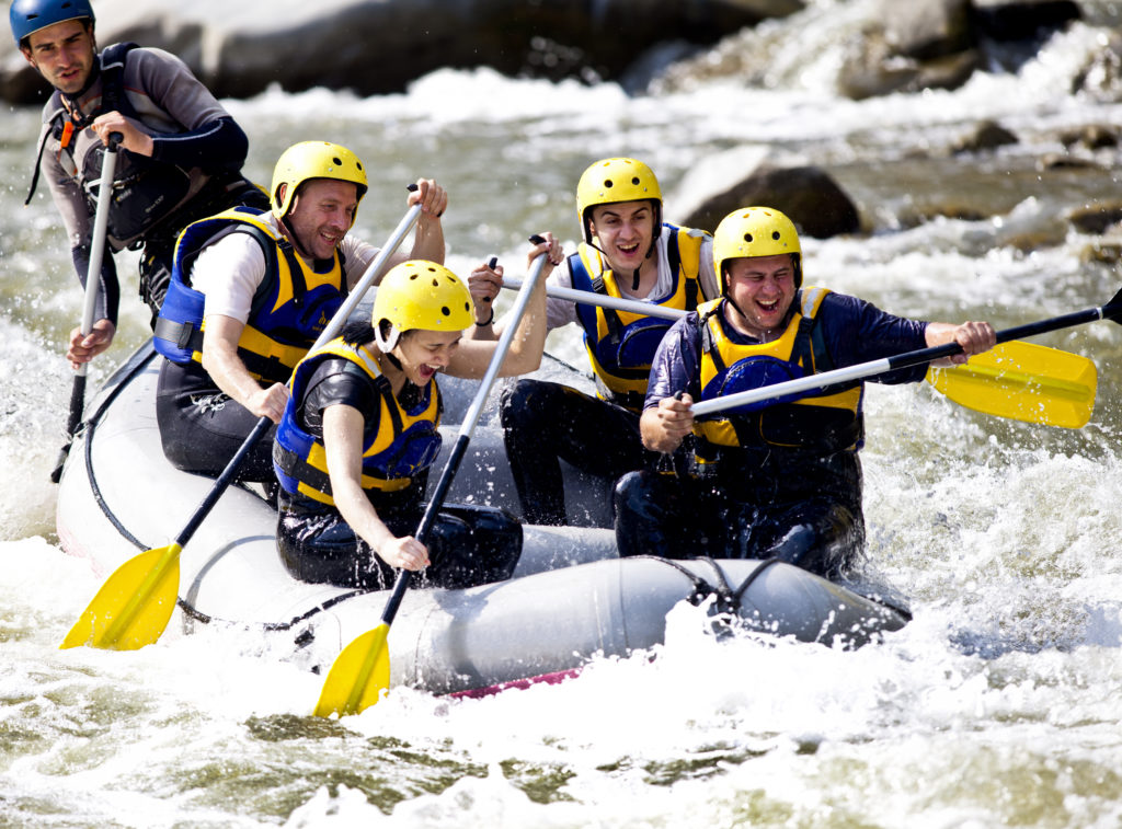 Group of happy people with guide whitewater rafting and rowing on river